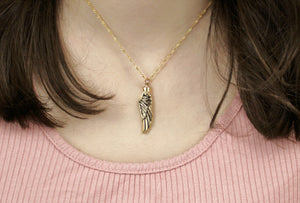 The Angel Wing Pet Urn Necklace, with a gold angel wing hanging vertically against the neck of the model with a gold chain.