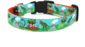 Dinosaur Dog Collar featuring orange webbing and a full design of T-Rex, Triceratops and Stegosaurus with a background of volcanoes, green hills and blue sky.