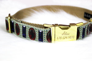 A dog collar designed to look like it’s studded with diamonds, rubies, and sapphires, with a gold engraved buckle option, sitting on white faux fur.